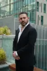 Nader Soussou in a dark suit, standing outside a glass building